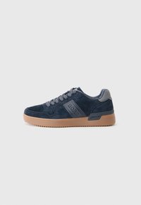 Baskets en daim bleu marine avec des lacets gris, logo "BORG" sur le côté et semelle en caoutchouc brun clair sur un fond blanc.