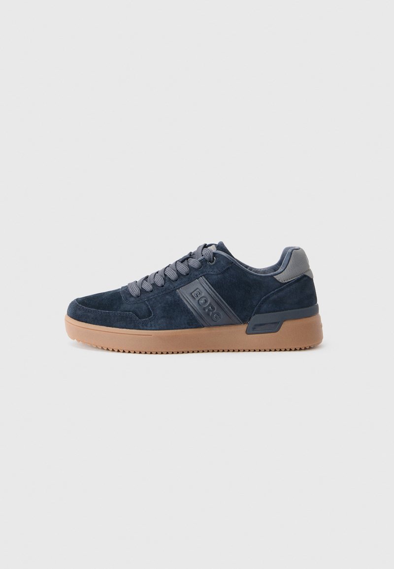 Baskets en daim bleu marine avec des lacets gris, logo "BORG" sur le côté et semelle en caoutchouc brun clair sur un fond blanc.