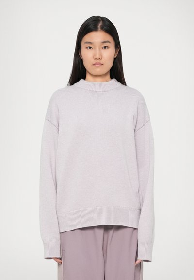 Pull surdimensionné lilas clair avec un col montant, des poignets et un ourlet côtelés. Fabriqué en tissu tricoté texturé, associé à un pantalon ample.
