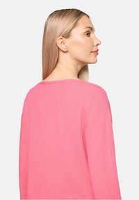 Pull en maille rose à col large, avec une coupe décontractée et des manches longues, mettant en valeur une texture fine et des détails subtils dans le tissu.
