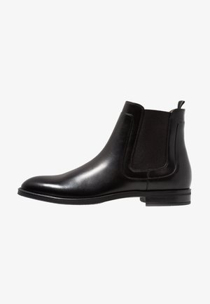 Botte Chelsea en cuir noir avec panneaux latéraux élastiques, bout arrondi et petit talon empilé. Surface lisse avec des détails de couture minimalistes.