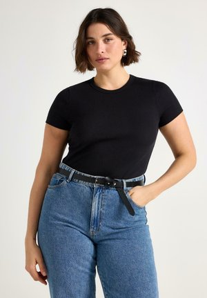 T-shirt nera a coste con maniche corte, abbinata a jeans di denim chiaro a vita alta e cintura nera. Design semplice e aderente.