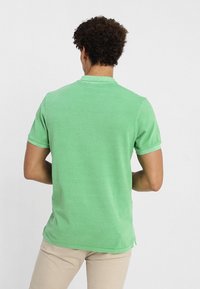 Zielona koszulka polo z krótkim rękawem, wykonana z bawełny o teksturowanym wykończeniu. Posiada klasyczny kołnierzyk i boczne rozporki u dołu.