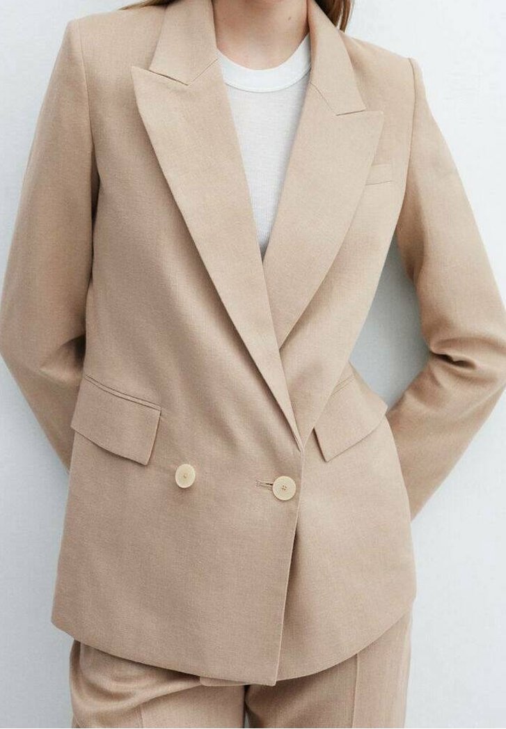 Blazer beige à double boutonnage avec revers crantés, deux poches avant et boutons crème, fabriqué en tissu texturé. Design simple et sur mesure.