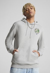 Grå hættetrøje lavet af blødt stof, med en kængurulomme, ribbede manchetter og et rundt logo-patch på brystet. Casual pasform med snoretræk.