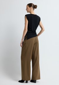 Černý bezrukávový top s volným střihem a bočními rozparky, kombinovaný s vysokými hnědými kalhotami s širokými nohavicemi a černými podpatkovými botami.