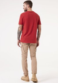 Camiseta roja de manga corta, de corte relajado, combinada con pantalones cargo beige claros que tienen bolsillos laterales y un dobladillo enrollado, complementados con calzado marrón claro.