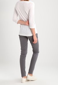 Top blanco de manga larga con escote redondo y puños doblados, combinado con pantalones ajustados grises y zapatillas blancas. Telas sencillas y ligeras.
