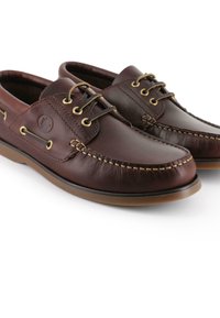 Zapatos de piel marrón con punta redondeada, costuras decorativas, ojales dorados y suela de goma. Presentan un logo en el lateral.