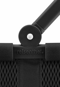 Detail einer schwarzen Netzstofftasche, mit einem runden schwarzen Connector und einem silbernen Metallknopf, auf der Seite befindet sich das eingeprägte "reisenthel"-Logo.