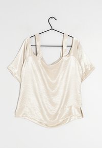 Top color crema a maniche corte con una superficie morbida e lucida. Presenta due spalline larghe e una vestibilità ampia e drappeggiata con spacchi laterali all'orlo.