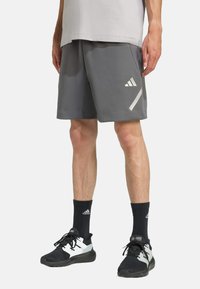 Grå sportsshorts i et tekstureret stof, med en hvid diagonalt stribe og logoaccenter. Bæres med sorte sokker og sko.