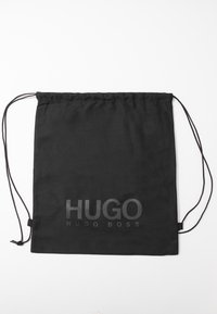 Sac en tissu noir avec cordons fins et inscription "HUGO HUGO BOSS" imprimée en grandes lettres gris foncé sur le devant.
