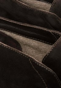 Wnętrze brązowego zamszowego buta z miękkim filcowym wykończeniem i widocznymi detalami szycia. Projekt podkreśla teksturę i kontrast materiałów.