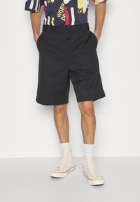 Sorte shorts lavet af letvægtsstof, midt-lår længde, med en afslappet pasform. Parret med hvide højhalsede sneakers og stribede sokker.