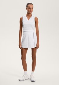 Witte mouwloze poloshirt met een tekstuurpatroon, gecombineerd met een witte rok met een zijknop en contrasterende bies aan de zoom.