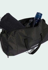 Black duffel bag made of textured fabric, with two carrying handles. Contains a rolled black towel, a blue water bottle, and a small accessory.