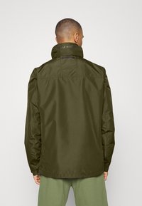 Veste imperméable vert olive avec un col haut et un logo au dos. Présente une texture lisse et des poignets réglables.