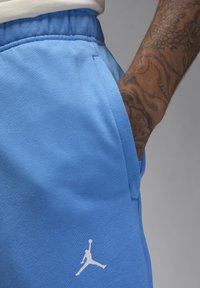 Modré športové šortky vyrobené z mäkkej látky majú na ľavej strane biely logo Jumpman a bočné vrecká so šitými detailmi.