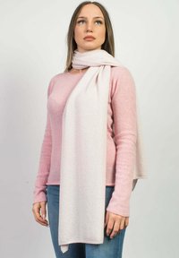 Lys pink tørklæde lavet af blødt stof, draperet om halsen, bæres med en lys pink sweater og blå jeans mod en ensfarvet baggrund.