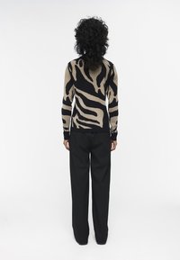 Gebreide trui met een beige en zwarte zebra print, gecombineerd met losse zwarte broeken. Geweven stof, lange mouwen en een ronde hals.