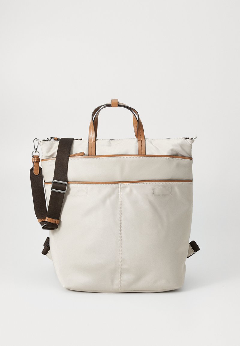 Sac fourre-tout beige clair avec des accents en cuir marron, anses supérieures et une bandoulière réglable marron foncé. Fermeture éclair avec poche avant.