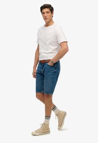 Shorts de mezclilla, de lavado claro, a la altura de la rodilla. Camiseta de algodón blanca, de cuello redondo. Zapatillas beige con acentos grises, combinadas con calcetines a rayas blancas y grises.