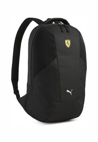 Sac à dos noir en nylon texturé. Présente des accents en maille, des écussons de logo (Ferrari et Puma), et des bretelles rembourrées et réglables.