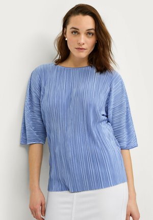 Top de color azul claro con pliegues, cuello redondo y mangas de longitud hasta los codos, con una textura suave y un corte relajado.