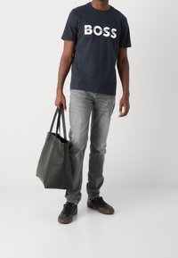 Marinblå bomull t-shirt med vit "BOSS" logotyp, grå denimjeans, svart läder tote-väska och mörka sneakers med bruna detaljer.