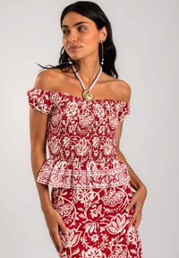 Top peplum rojo y blanco con hombros al descubierto, con patrones florales, cuerpo fruncido y mangas abullonadas. Se lleva con una falda a juego con patrones.