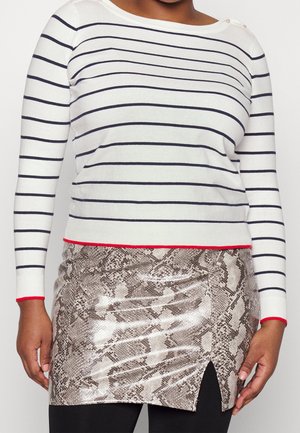 Woman wearing a white long-sleeve shirt with black stripes and a short, shiny snakeskin-patterned skirt with a small front slit.