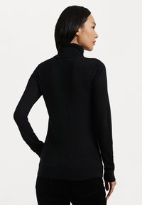 Črna turtleneck pulover iz mehkega pletenega materiala, z ozkim krojem, dolgimi rokavi in ribano teksturo na ovratniku in manšetah.