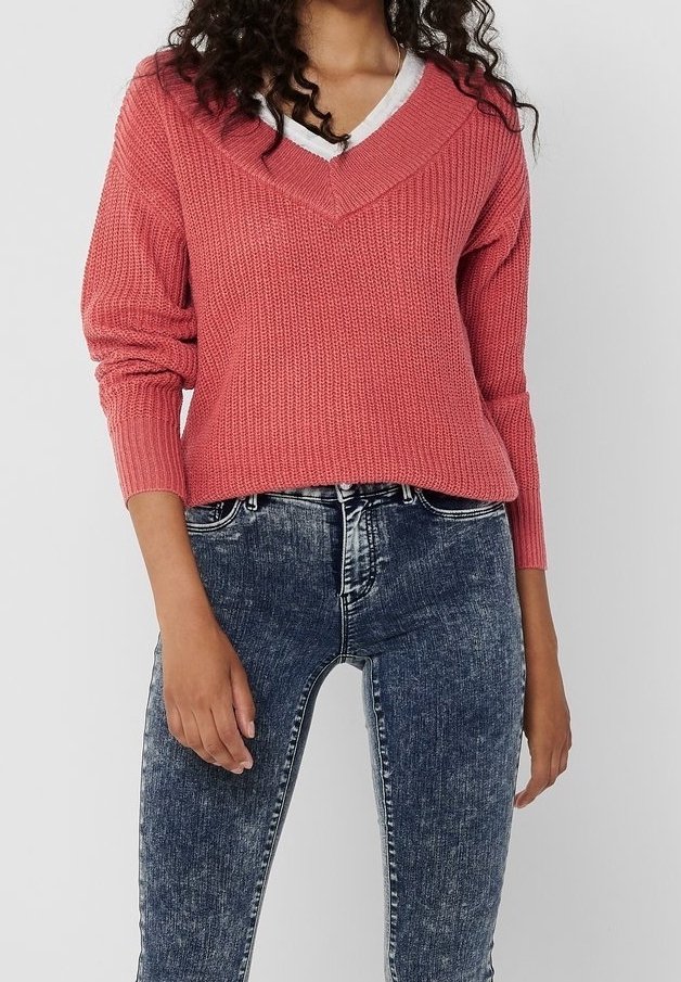 Roze gebreide trui met een V-hals, geribbelde textuur en lange mouwen, gecombineerd met een donkere skinny jeans.