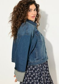 Giacca in denim di blu medio con una vestibilità cropped e maniche oversize. Presenta due tasche frontali e accenti grigi ai polsini.