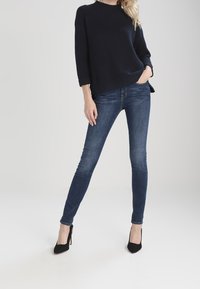 Dark navy ribbed knit sweater paired with fitted blue jeans and black high-heeled shoes, showcasing a streamlined silhouette.