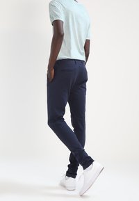 Navy blue stretch chinos with slim fit, featuring back pockets and wear-resistant fabric. Pairing with white sneakers, light teal T-shirt.