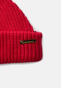 Czerwona dziana czapka beanie o prążkowanej fakturze. Posiada czarną prostokątną metkę z złotym napisem "Barbour."