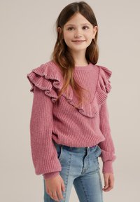 Rosa stickad tröja med volangärmar, texturerad tyg och ribbade ärmmuddar. Matchad med ljusblå jeans.