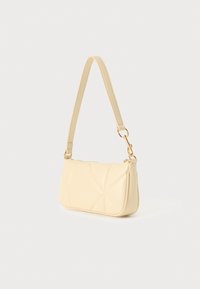 Μπεζ τσάντα χειρός από συνθετικό δέρμα με γεωμετρικό ραμμένο σχέδιο, μονή λαβή και μεταλλικά στοιχεία σε χρυσό τόνο. Συμπαγές ορθογώνιο σχήμα.