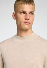 Maglione a maglia beige chiaro con un collo alto e rigato e maniche corte. Morbido al tatto e con sottili variazioni nel tessuto.