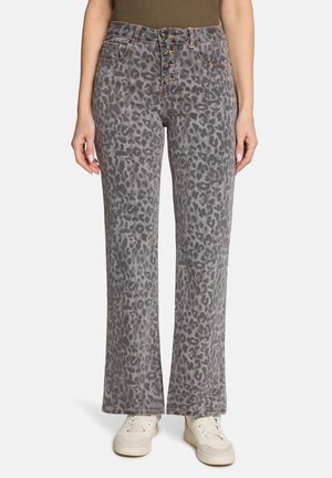 Szare dżinsy w panterkę z zapięciem na guziki, proste nogawki, noszone z jasnobeżowymi trampkami i oliwkowo-zieloną bluzką.