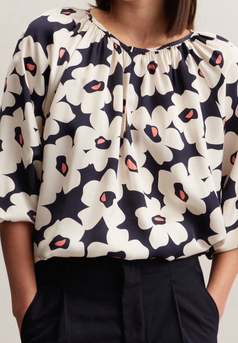 Blusa a stampa floreale in navy, bianco e corallo, con scollatura arricciata e vestibilità rilassata. Pattern di fiori vibranti e morbida texture del tessuto.