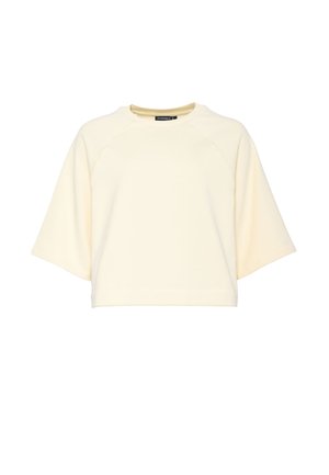 Kermanvärinen, lyhythihainen lyhyt collegepaita pyöreällä pääntiellä ja raglansaumoilla, esillä valkoisella taustalla.