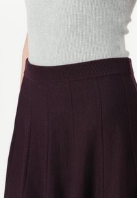 Haut en tricot gris avec une texture côtelée au-dessus d'une jupe plissée bordeaux présentant des rayures verticales et une taille élastique ajustée.