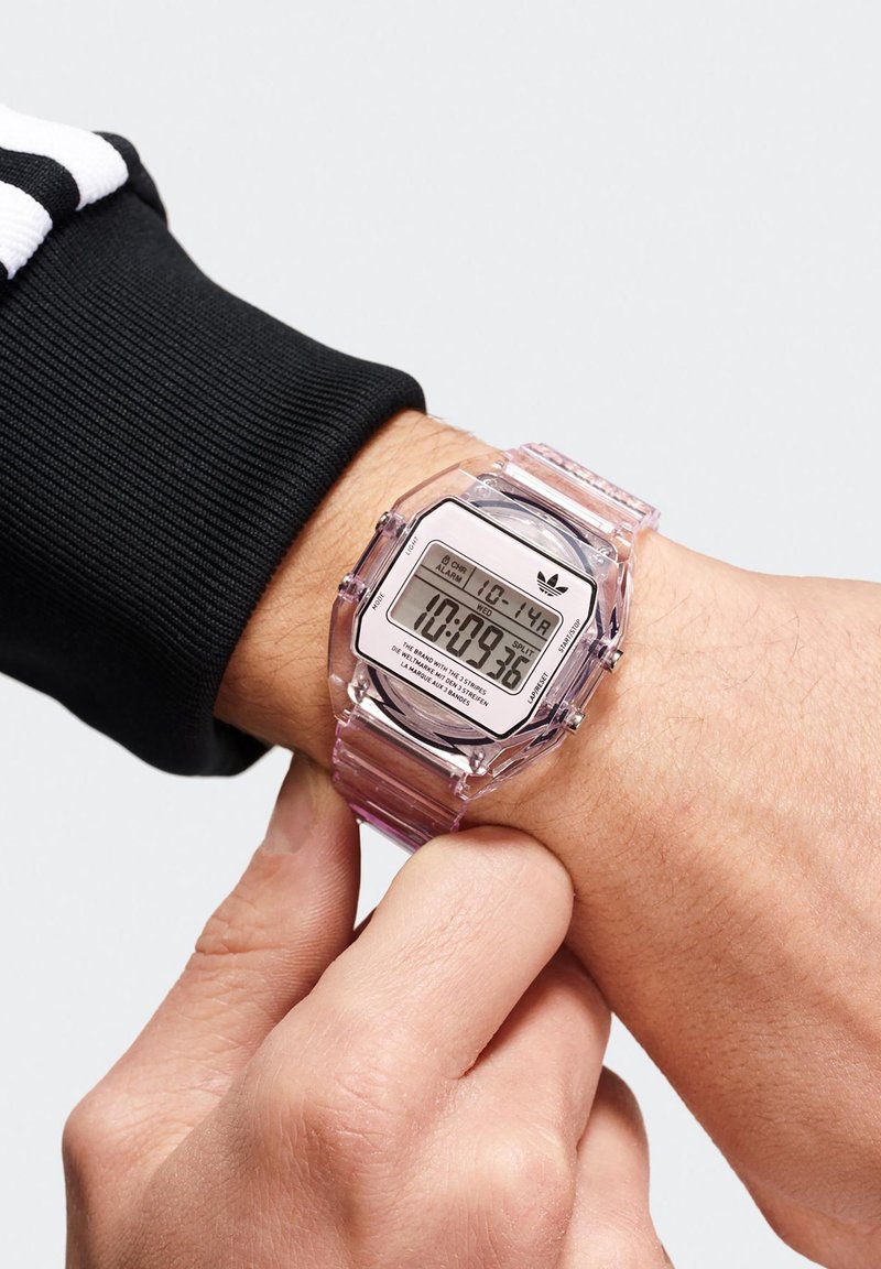 Reloj digital con una correa de plástico transparente y una esfera octagonal, que presenta una gran pantalla digital y detalles en negro. Manos ajustando la hora.