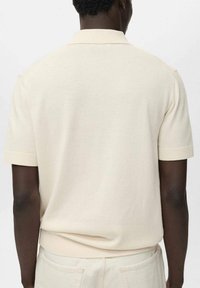 T-paita lyhyillä hihoilla, vaaleanbeige, ribbireunuksella varustettu kaulus ja hihansuut, pehmeä neulepinta ja suora helma. Takakuvassa yksinkertainen ja minimalistinen muotoilu.