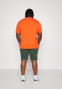 Pomarańczowa koszulka z krótkim rękawem połączona z zielonymi szortami. Koszulka ma prosty design, podczas gdy szorty są dopasowane i mają gładką fakturę.
