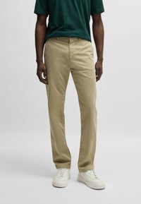 Pantalones de algodón beige con corte recto, que presentan bolsillos delanteros, costuras sutiles y se combinan con zapatillas blancas.