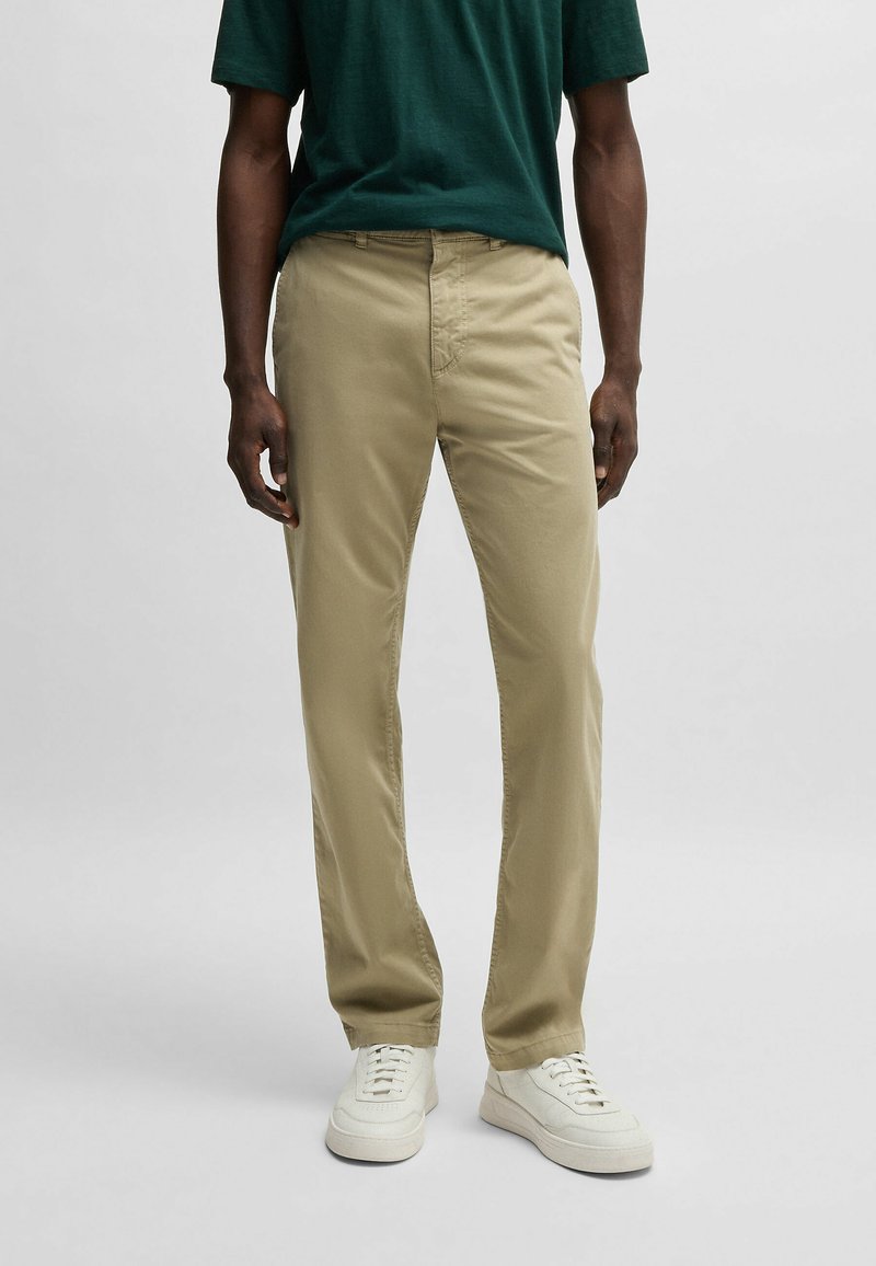 Pantalones de algodón beige con corte recto, que presentan bolsillos delanteros, costuras sutiles y se combinan con zapatillas blancas.
